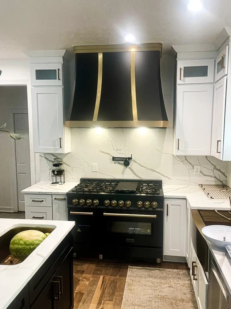 Black powder coated range hood with a single brass strap above a black range, between white wall cabinets.