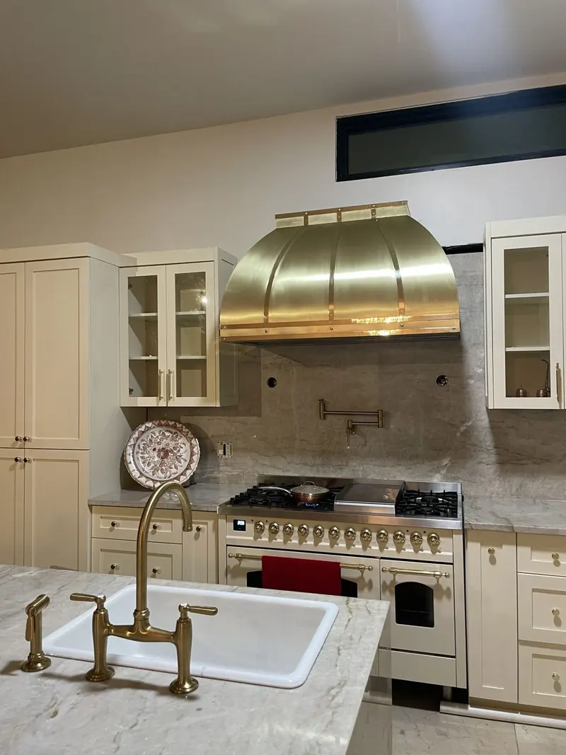 Brass Campo range hood with banded straps above a range, against a stone backsplash in a Miami, Florida kitchen