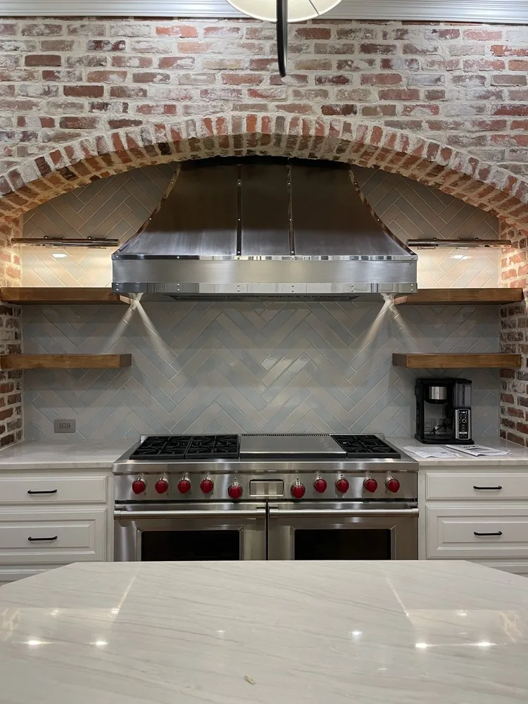 Brushed stainless steel range hood set inside an exposed brick arch above a professional range.