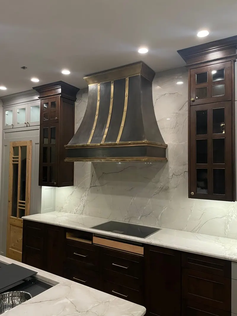 Dark Monarch range hood with brass banding against a marble backsplash in a Southlake, Texas kitchen